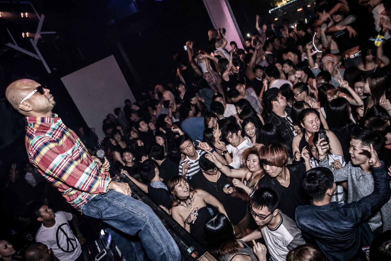 DJ Kzee performing above a packed nightclub crowd